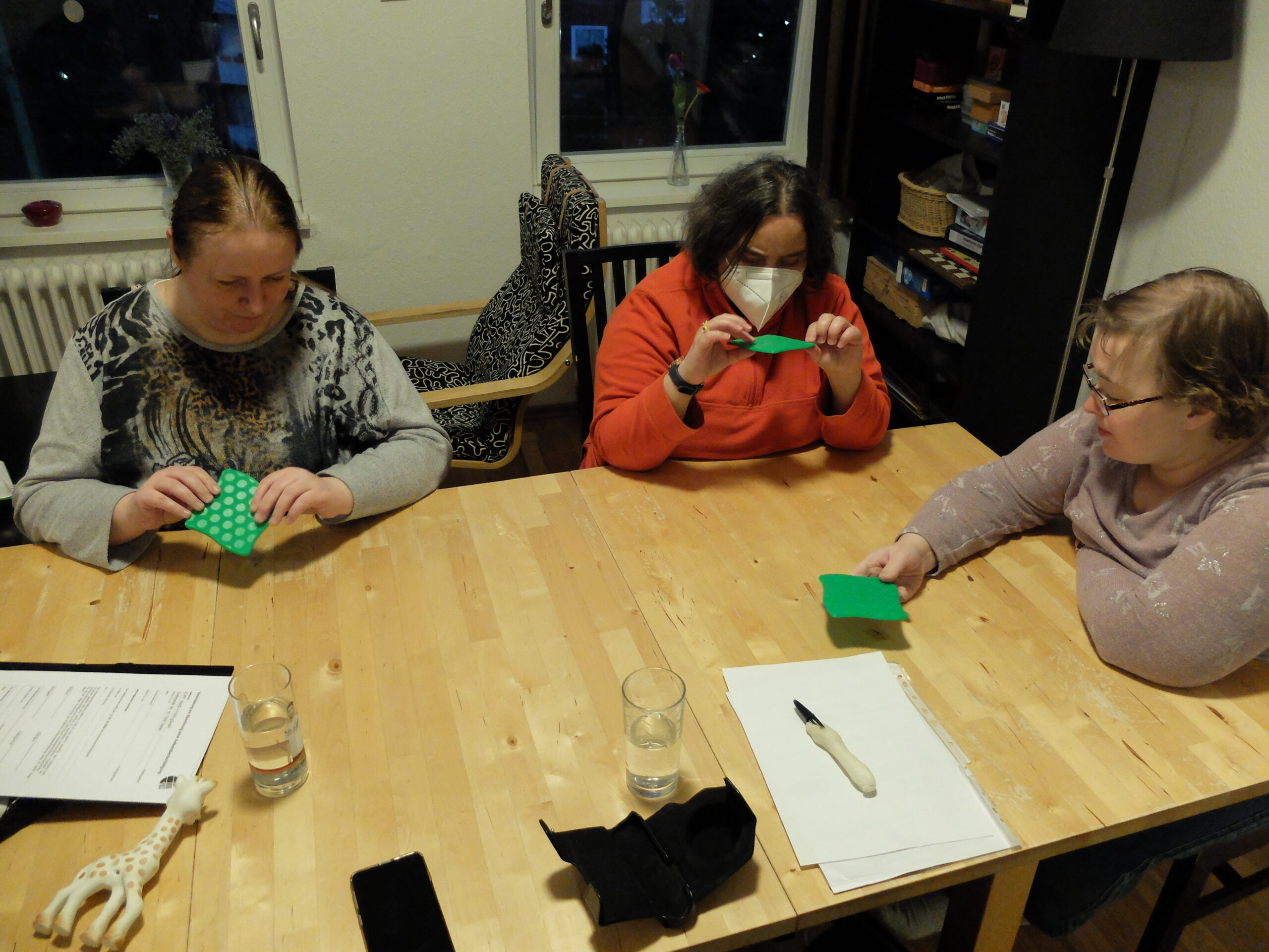 Foto von Drei Frauen die um einen Tisch herum sitzen und grüne Karten in den Händen halten